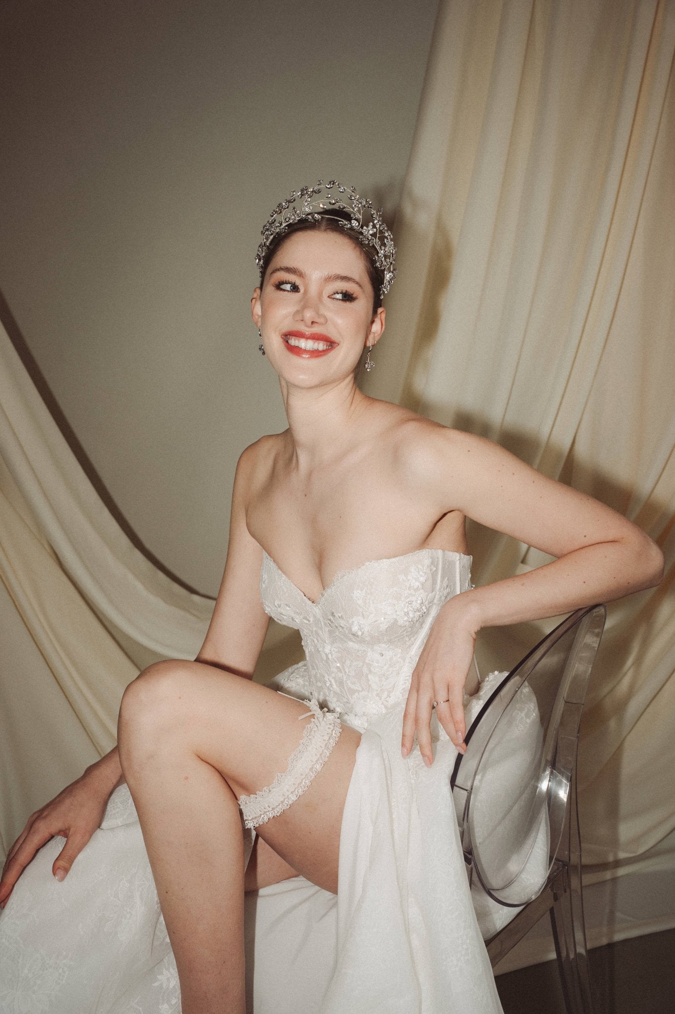 bride wears sparkling crystal tiara, smiling broadly while showing her garter through a slit in her ballgown