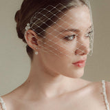 Bride wears a short merry widow mask birdcage veil with Perla pearl cluster hair pins and Dina Short gold round pearl stud drop earrings