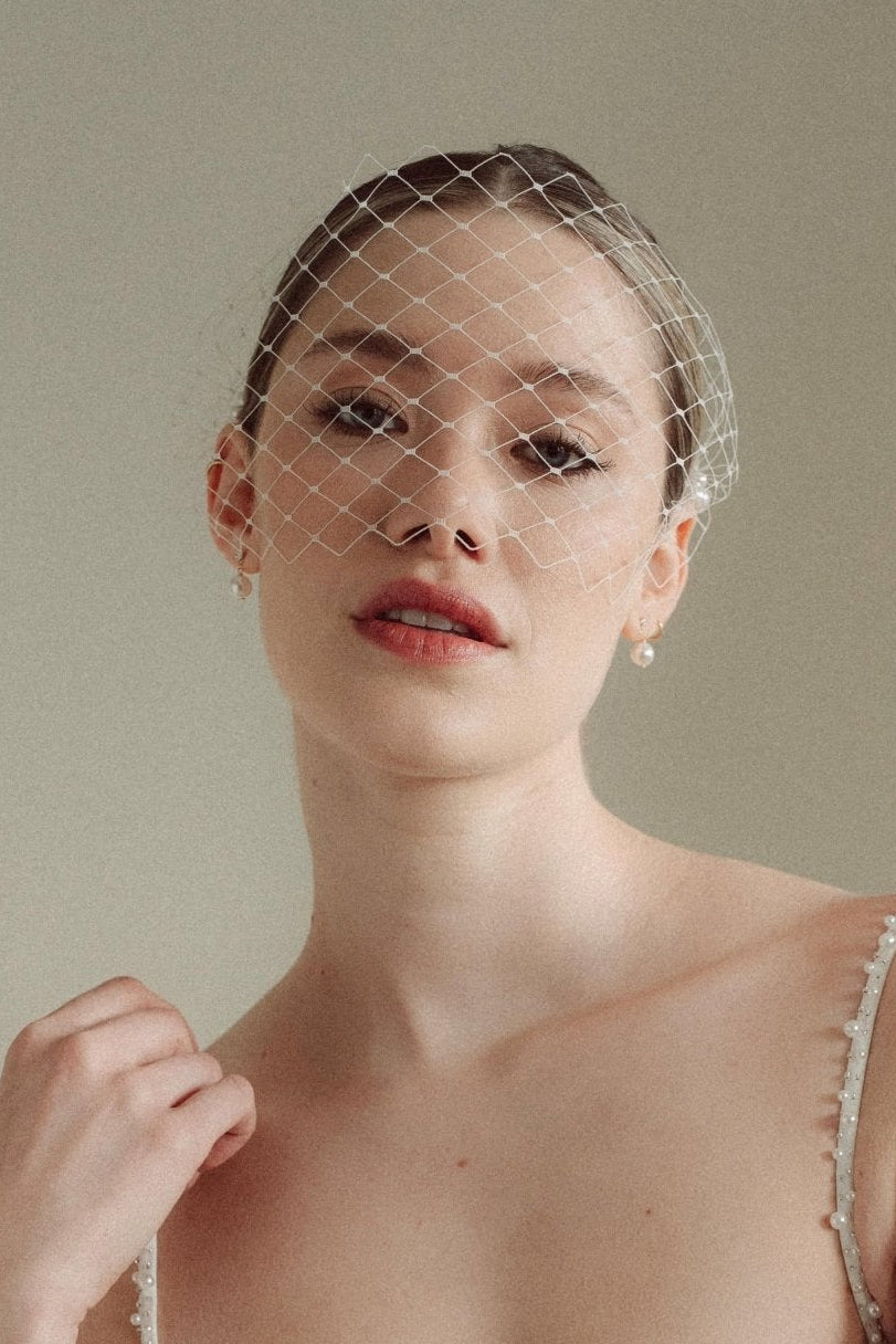 Bride wears a short merry widow mask birdcage veil with Perla pearl cluster hair pins and Dina Short gold round pearl stud drop earrings