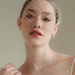 Bride wears a short merry widow mask birdcage veil with Perla pearl cluster hair pins and Dina Short gold round pearl stud drop earrings