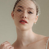 Bride wears a short merry widow mask birdcage veil with Perla pearl cluster hair pins and Dina Short gold round pearl stud drop earrings