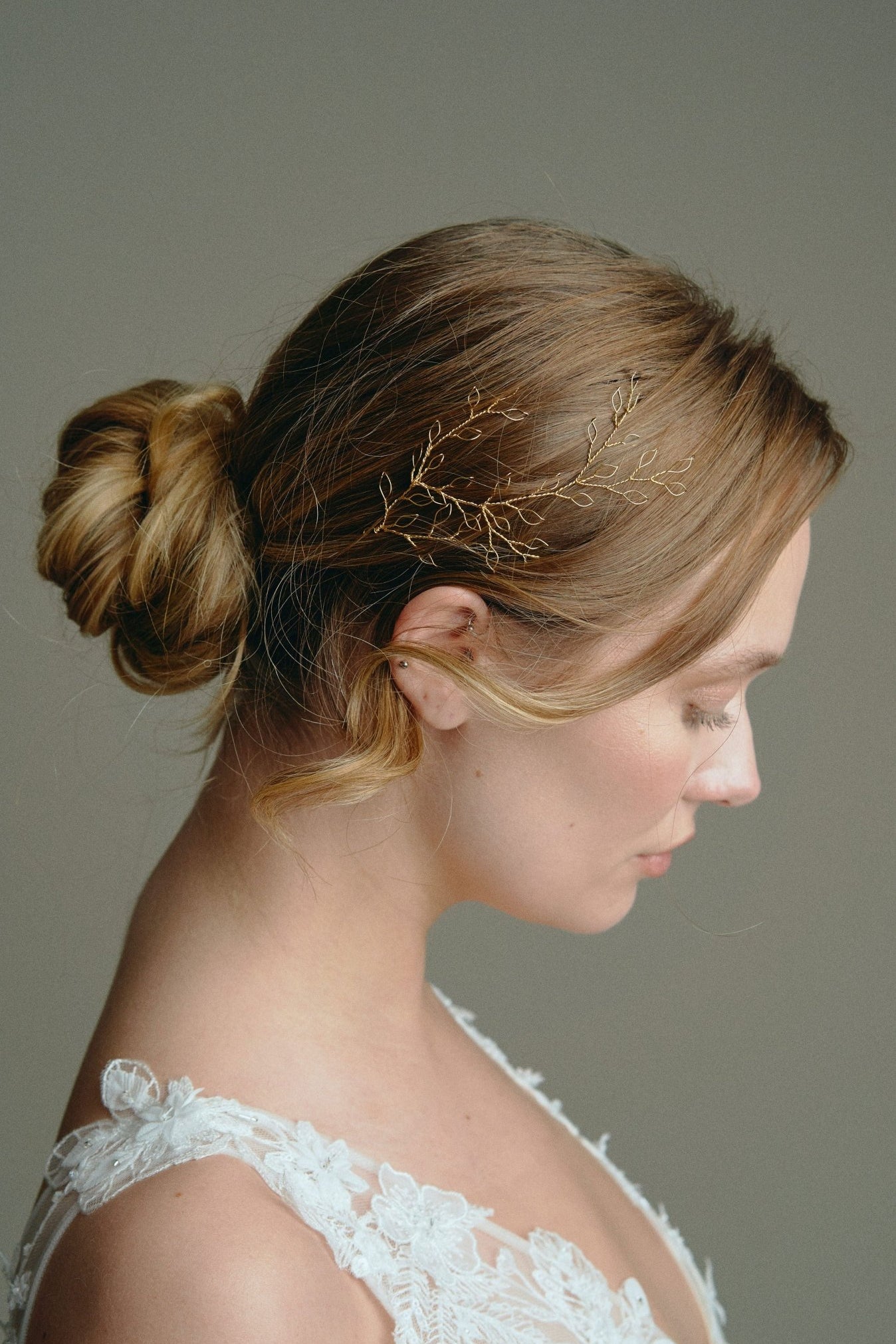 Wedding hair vine - model wears a gold leafy delicate hair vine above her ear with a low bun 