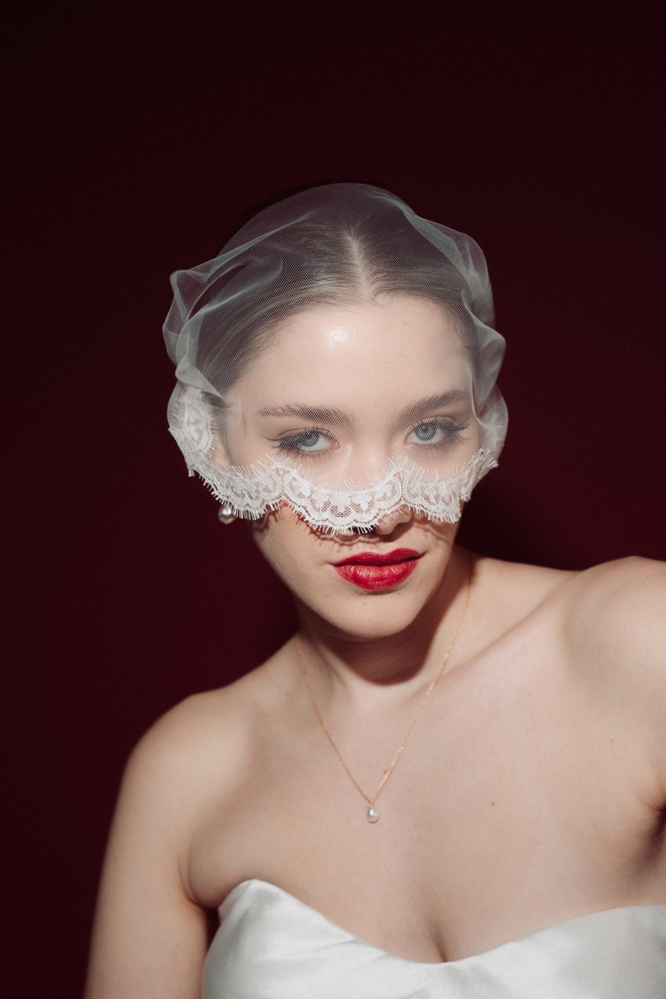 Woman wearing a sheer face veil with lace details against a dark background