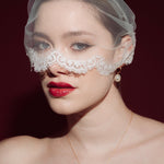 Woman wearing a sheer face veil with lace details against a dark background