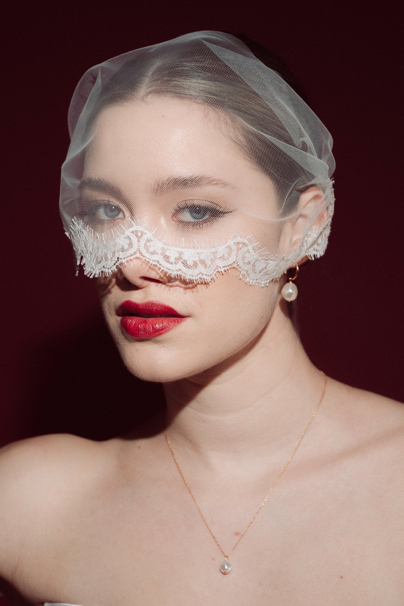 Woman wearing a sheer face veil with lace details against a dark background