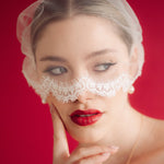 Woman wearing a lace edged mask style micro veil against a red background