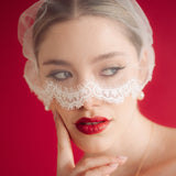 Woman wearing a lace edged mask style micro veil against a red background