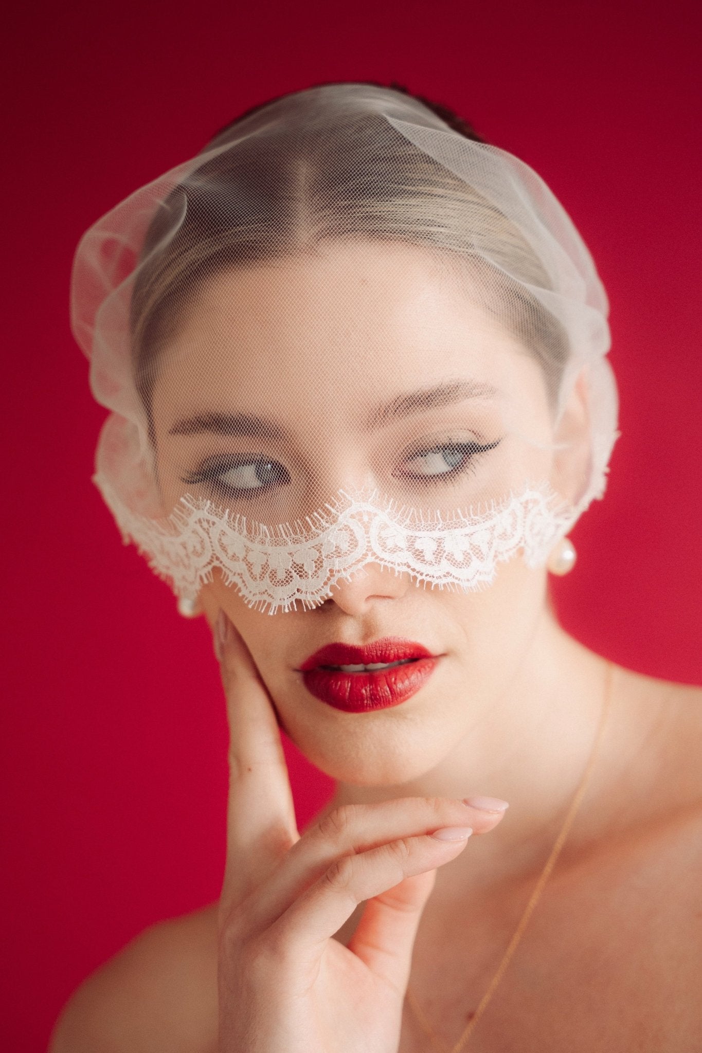 Woman wearing a lace edged mask style micro veil against a red background