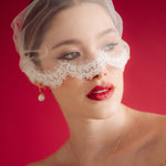 Woman wearing a sheer face veil with lace details against a red background