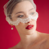 Woman wearing a sheer face veil with lace details against a red background