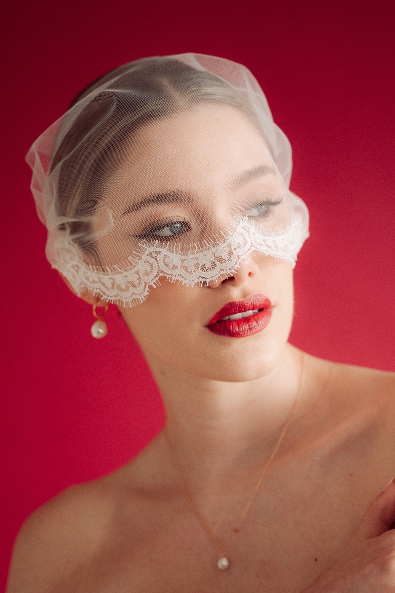 Woman wearing a sheer face veil with lace details against a red background