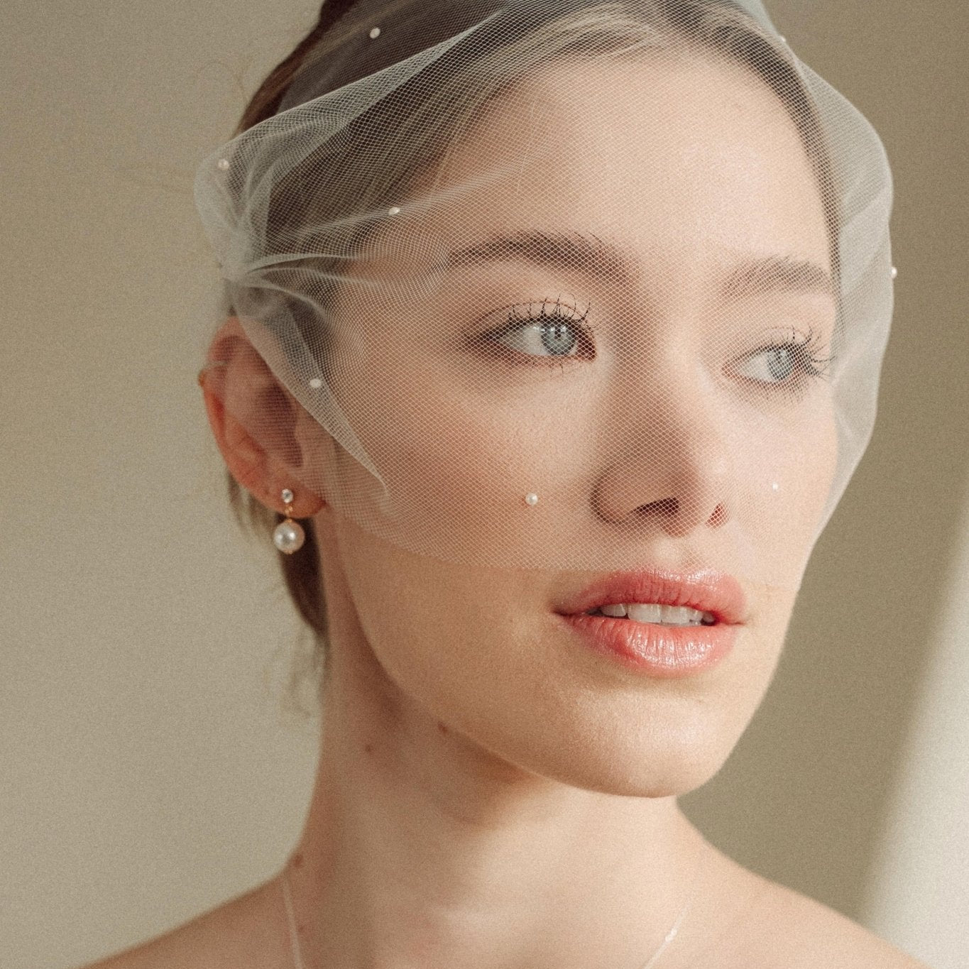 bride wears an ivory tulle mask style micro veil with small pearl embellishment with a baroque coin pearl necklace and crystl and pearl stud drop earring
