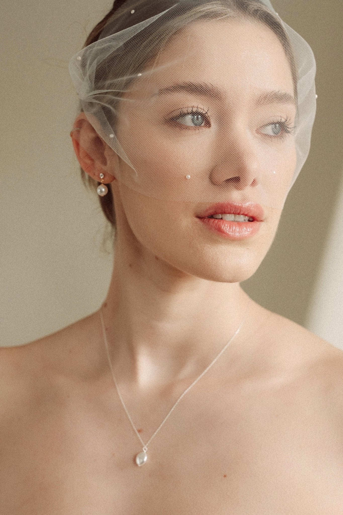 bride wears an ivory tulle mask style micro veil with small pearl embellishment with a baroque coin pearl necklace and crystl and pearl stud drop earring