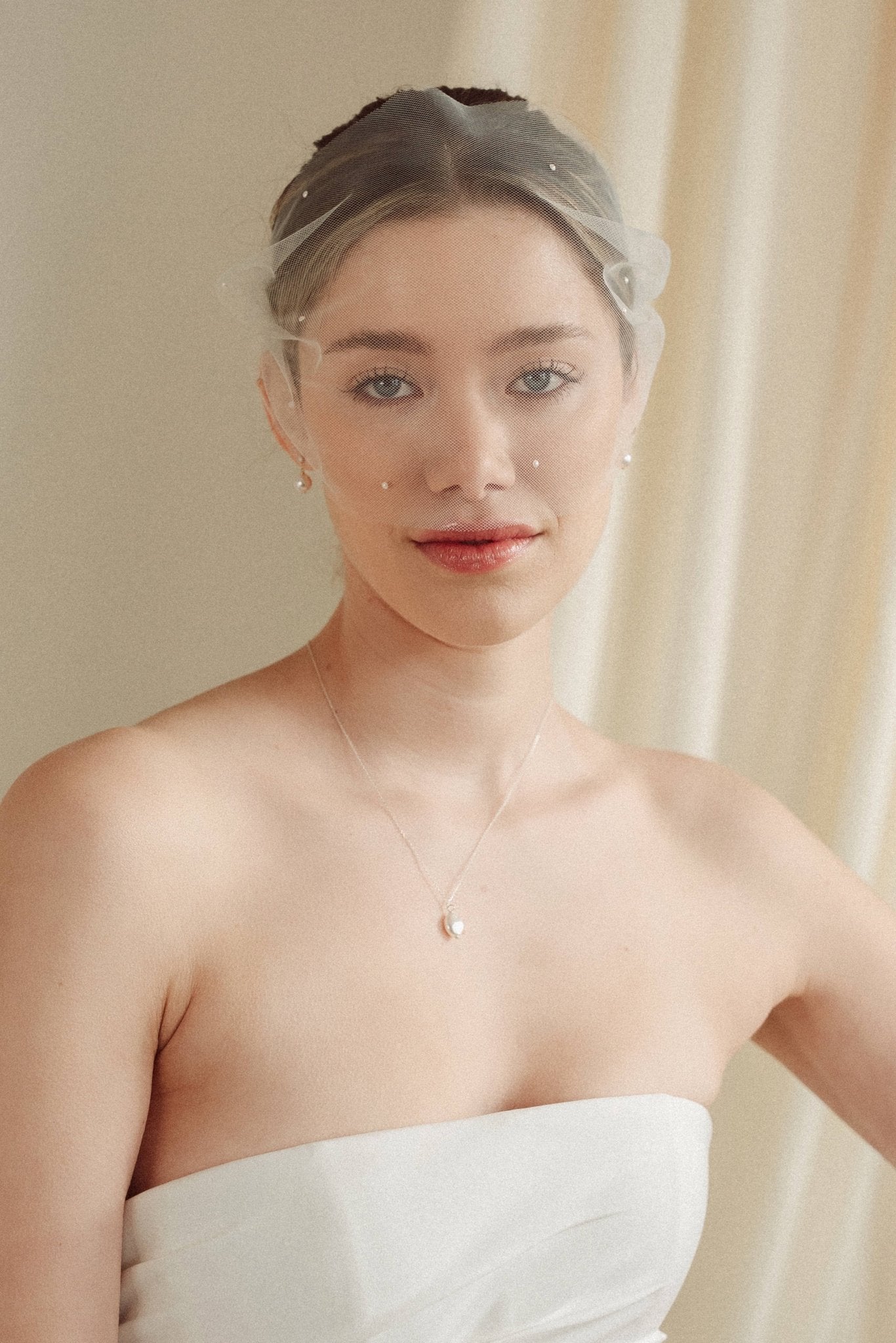 bride wears an ivory tulle mask style micro veil with small pearl embellishment with a baroque coin pearl necklace and crystl and pearl stud drop earring
