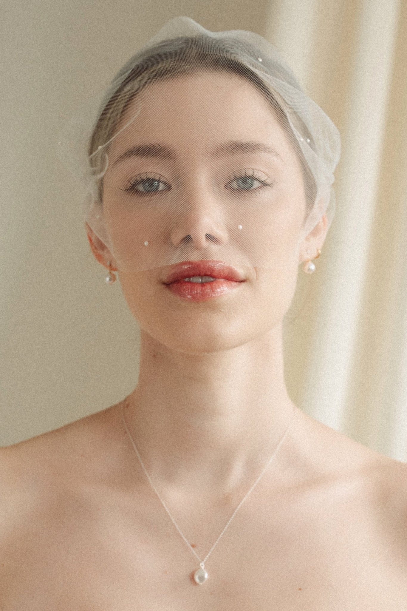 bride wears an ivory tulle mask style micro veil with small pearl embellishment with a baroque coin pearl necklace and crystl and pearl stud drop earring