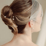 bride wears an ivory tulle mask style micro veil with small pearl embellishment with small pearl hair pins in a a soft chignon French twist updo and crystl and pearl stud drop earring