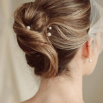 bride wears an ivory tulle mask style micro veil with small pearl embellishment with small pearl hair pins in a a soft chignon French twist updo and crystl and pearl stud drop earring