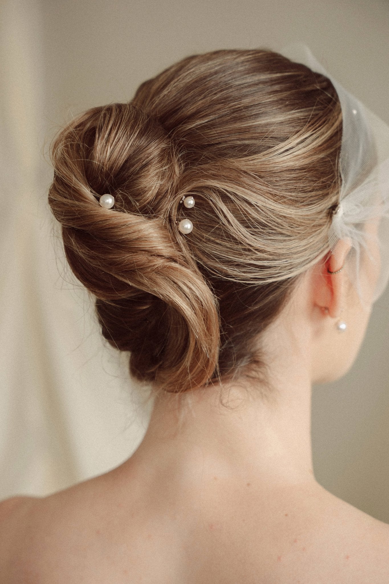 bride wears an ivory tulle mask style micro veil with small pearl embellishment with small pearl hair pins in a a soft chignon French twist updo and crystl and pearl stud drop earring