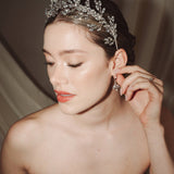 A bride wears a sparling silver crystal crown with hair pins positioned at it's base to create the effect of leaves growing out of the base of the headpiece she is adjusting her matching crystal drop earrings