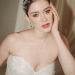 A bride wears a sparkling silver crystal crown with hair pins positioned at it's base to create the effect of leaves growing out of the base of the headpiece 