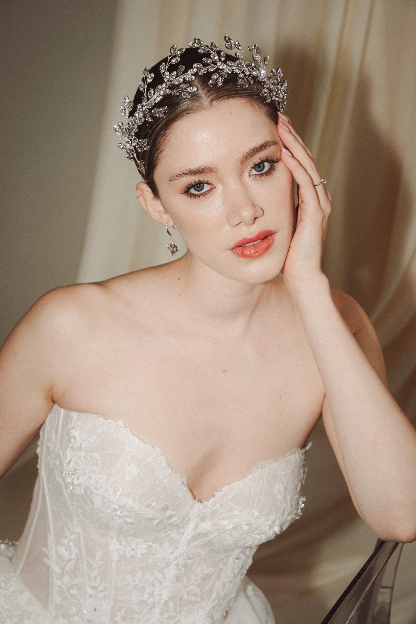 A bride wears a sparkling silver crystal crown with hair pins positioned at it's base to create the effect of leaves growing out of the base of the headpiece 