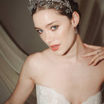 A bride wears a sparkling silver crystal crown with hair pins positioned at it's base to create the effect of leaves growing out of the base of the headpiece 
