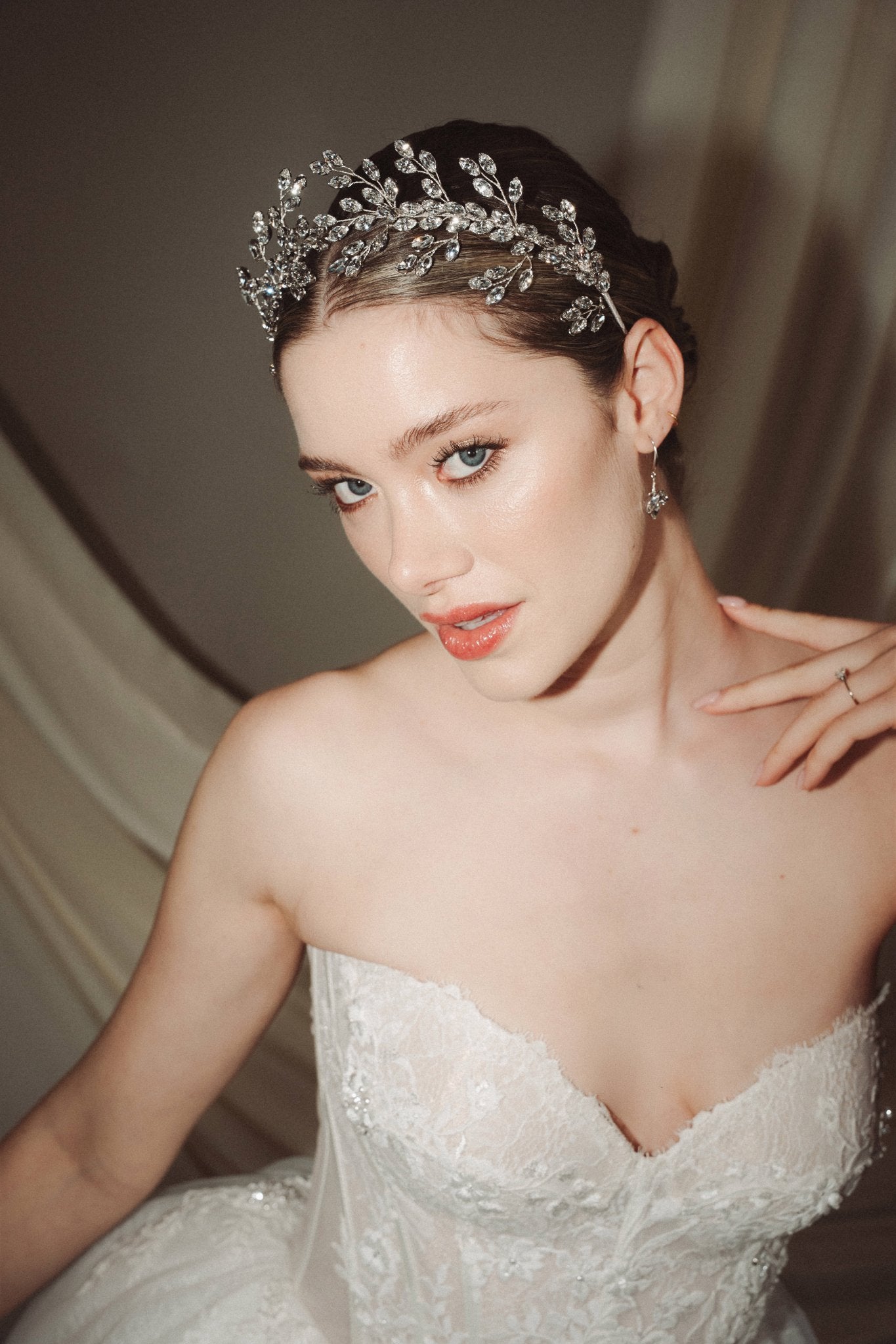 A bride wears a sparkling silver crystal crown with hair pins positioned at it's base to create the effect of leaves growing out of the base of the headpiece 