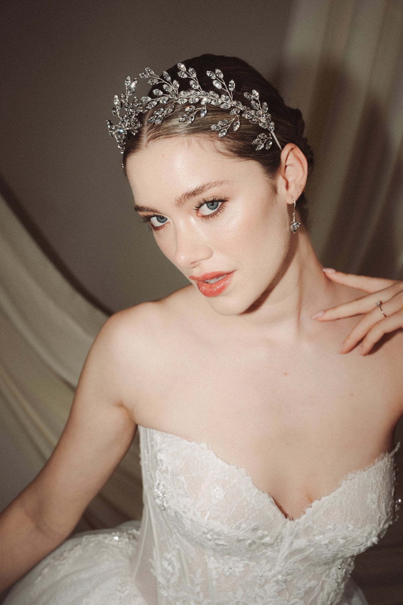A bride wears a sparkling silver crystal crown with hair pins positioned at it's base to create the effect of leaves growing out of the base of the headpiece 