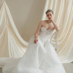 Woman in a strapless wedding dress reclines in front of a draped satin  backdrop wearing a sparkling silver crystal crown with hair pins positioned at it's base to create the effect of leaves growing out of the base of the headpiece 