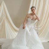Woman in a strapless wedding dress reclines in front of a draped satin  backdrop wearing a sparkling silver crystal crown with hair pins positioned at it's base to create the effect of leaves growing out of the base of the headpiece 