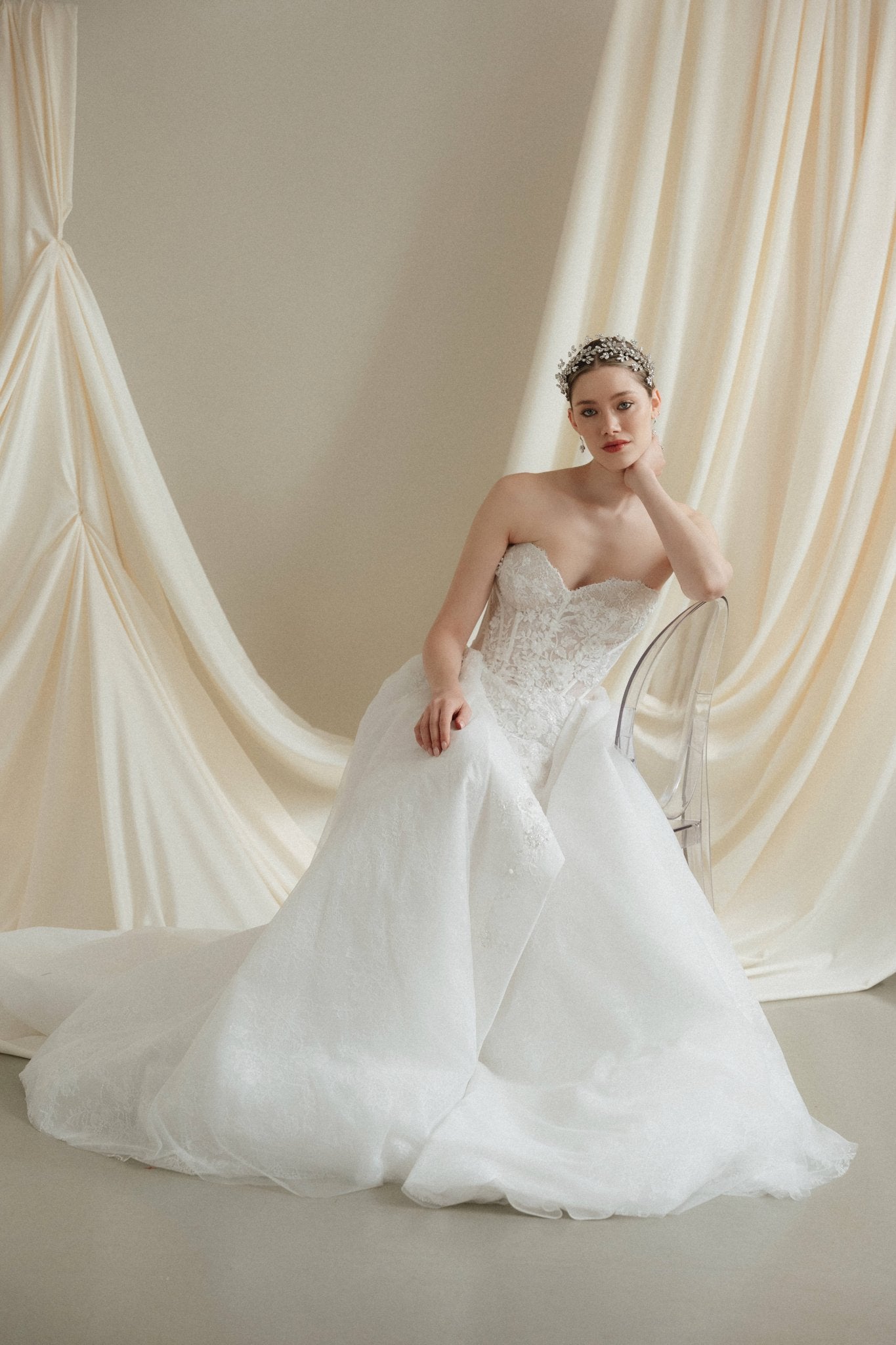 Woman in a strapless wedding dress reclines in front of a draped satin  backdrop wearing a sparkling silver crystal crown with hair pins positioned at it's base to create the effect of leaves growing out of the base of the headpiece 