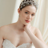 A bride wearing a sparkling silver crystal crown with hair pins positioned at it's base to create the effect of leaves growing out of the base of the headpiece 