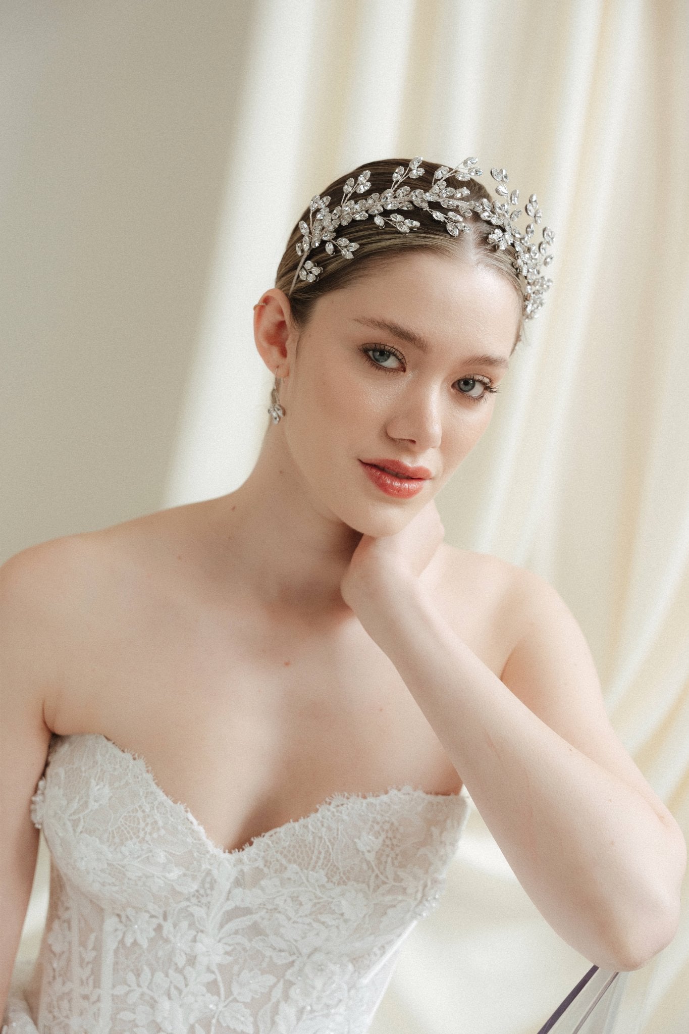 A bride wearing a sparkling silver crystal crown with hair pins positioned at it's base to create the effect of leaves growing out of the base of the headpiece 