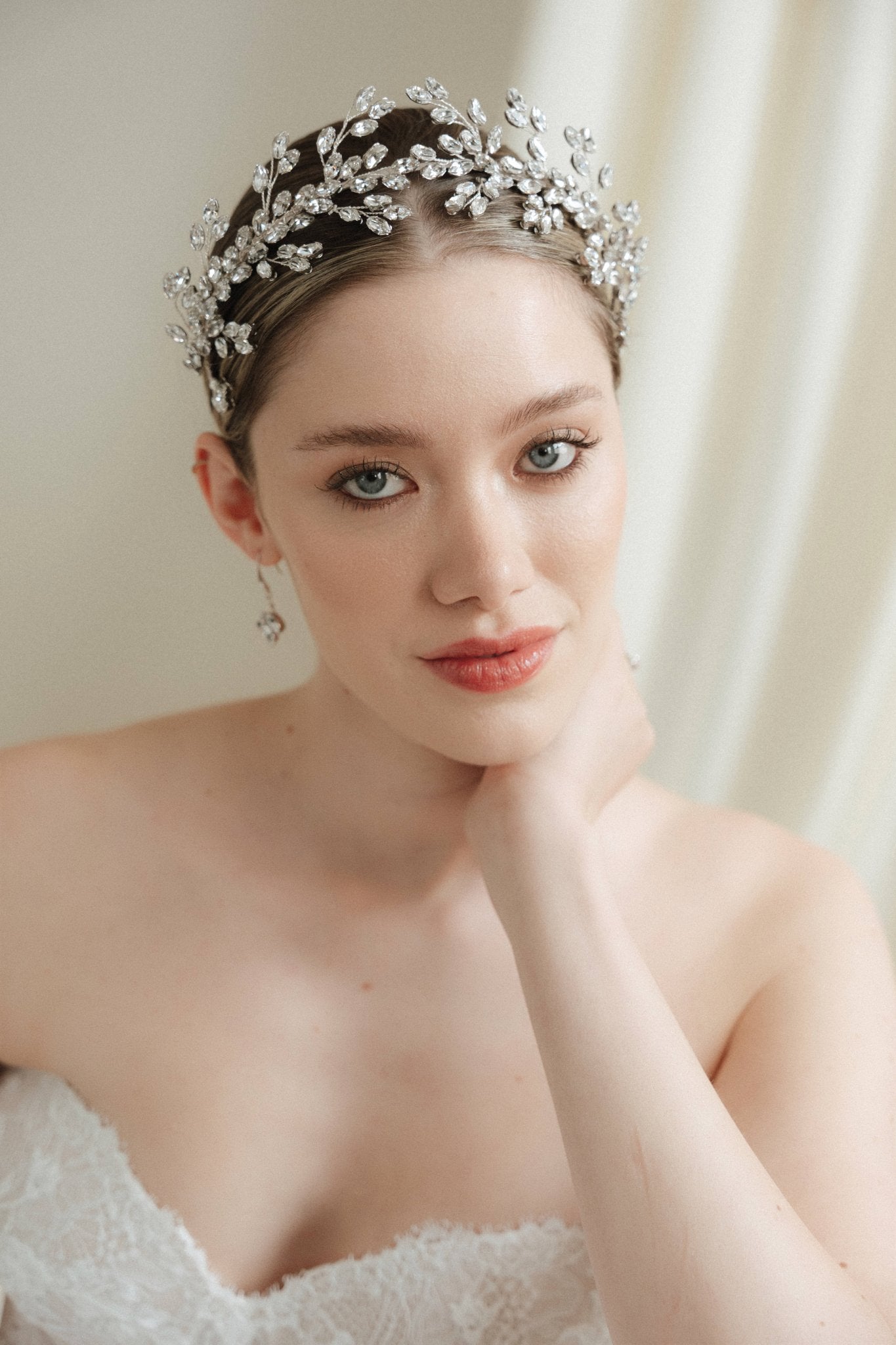 A bride wears a sparling silver crystal crown with hair pins positioned at it's base to create the effect of leaves growing out of the base of the headpiece 