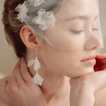 Bride wears an ivory tulle veil with face-framing silk flowers with coordinating silk flower and pearl long drop earrings
