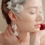 Bride wears an ivory tulle veil with face-framing silk flowers with coordinating silk flower and pearl long drop earrings