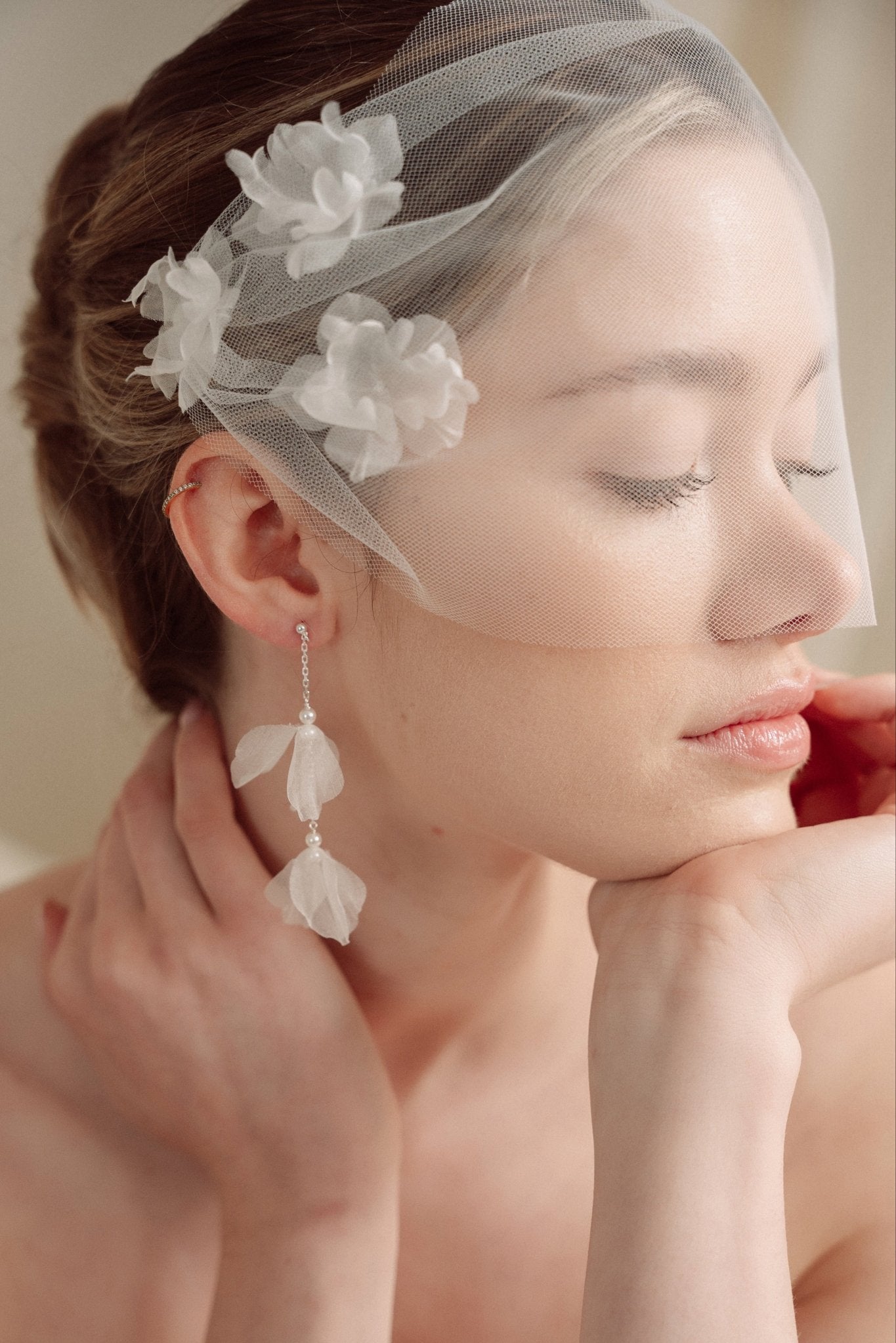 Bride wears an ivory tulle veil with face-framing silk flowers with coordinating silk flower and pearl long drop earrings