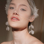 Bride wears an ivory tulle veil with face-framing silk flowers with coordinating silk flower and pearl long drop earrings