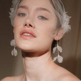 Bride wears an ivory tulle veil with face-framing silk flowers with coordinating silk flower and pearl long drop earrings