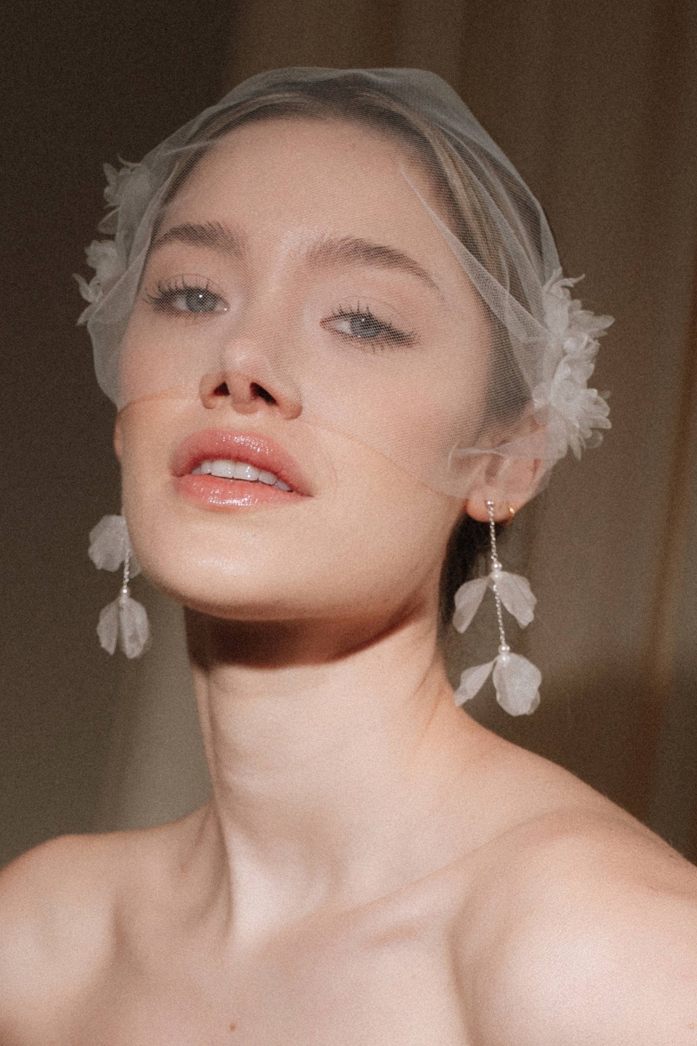 Bride wears an ivory tulle veil with face-framing silk flowers with coordinating silk flower and pearl long drop earrings