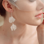 Bride wears an ivory tulle veil with face-framing silk flowers with coordinating silk flower and pearl long drop earrings