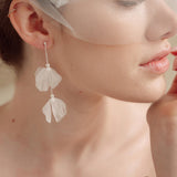Bride wears an ivory tulle veil with face-framing silk flowers with coordinating silk flower and pearl long drop earrings