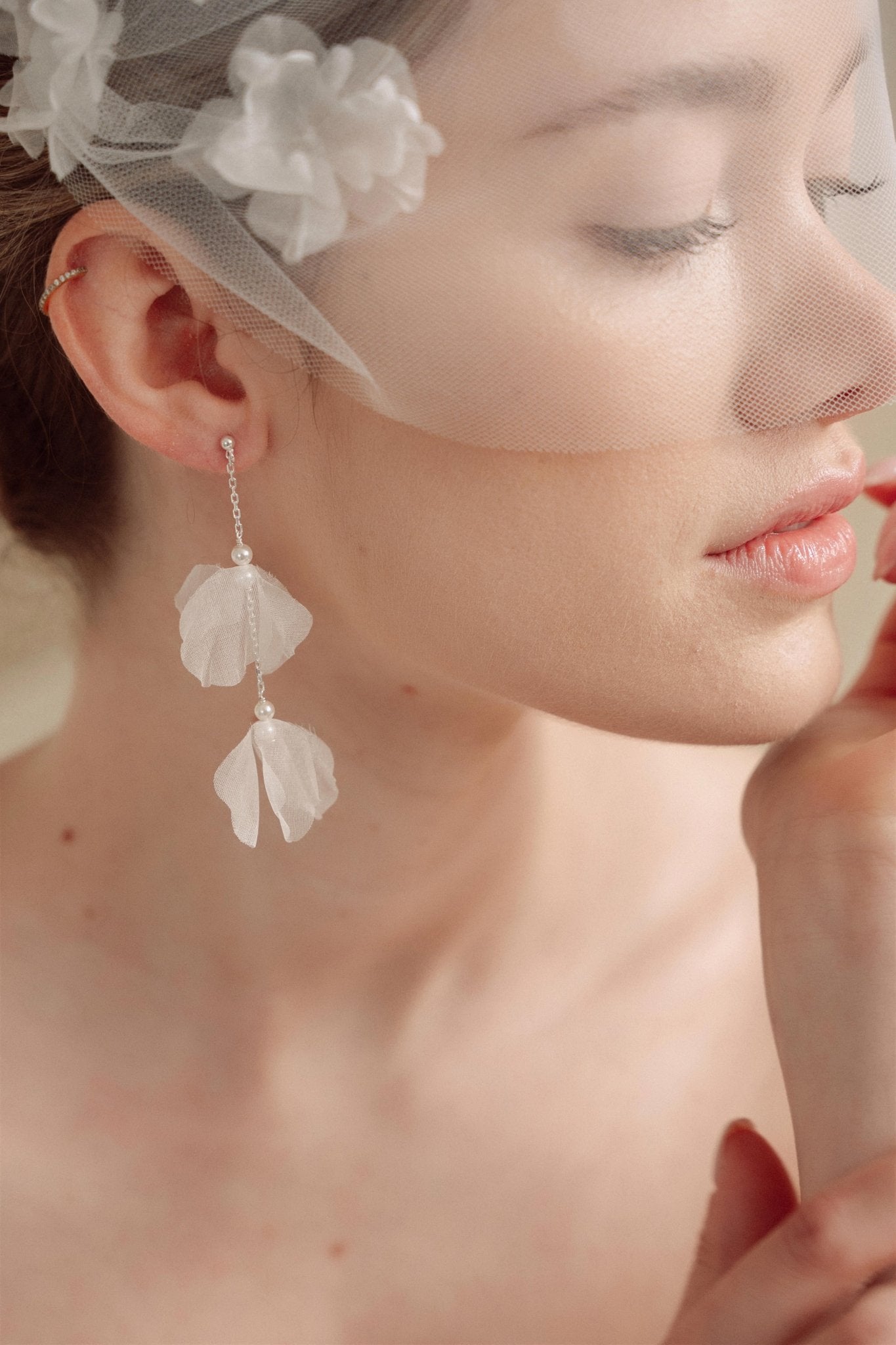 Bride wears an ivory tulle veil with face-framing silk flowers with coordinating silk flower and pearl long drop earrings