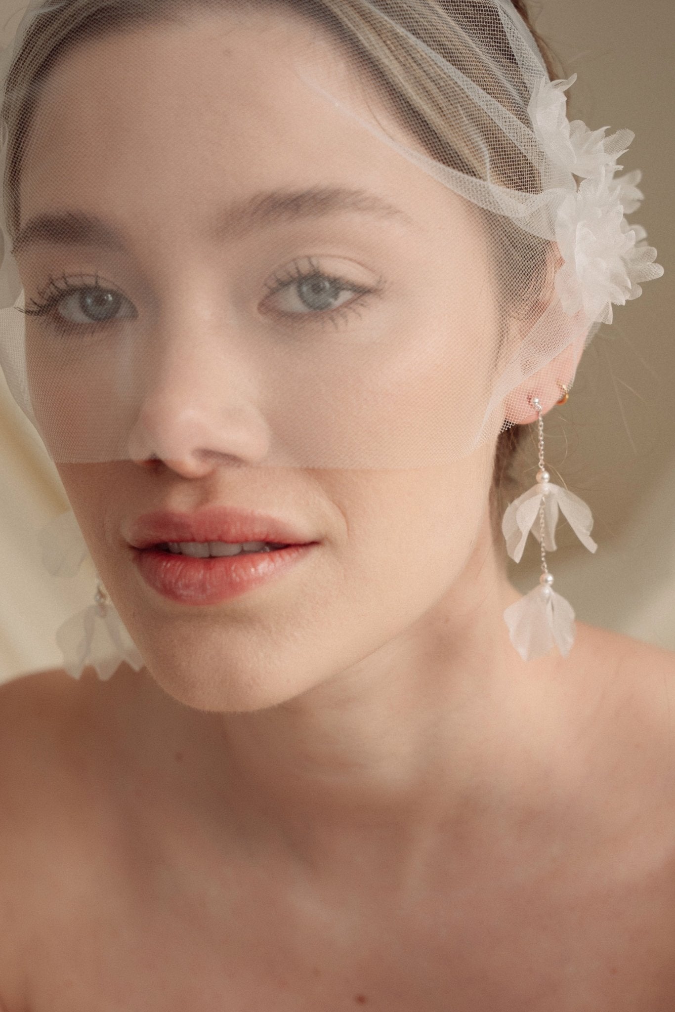 Bride wears an ivory tulle veil with face-framing silk flowers with coordinating silk flower and pearl long drop earrings