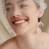 Bride wears an ivory tulle veil with face-framing silk flowers with coordinating silk flower and pearl long drop earrings