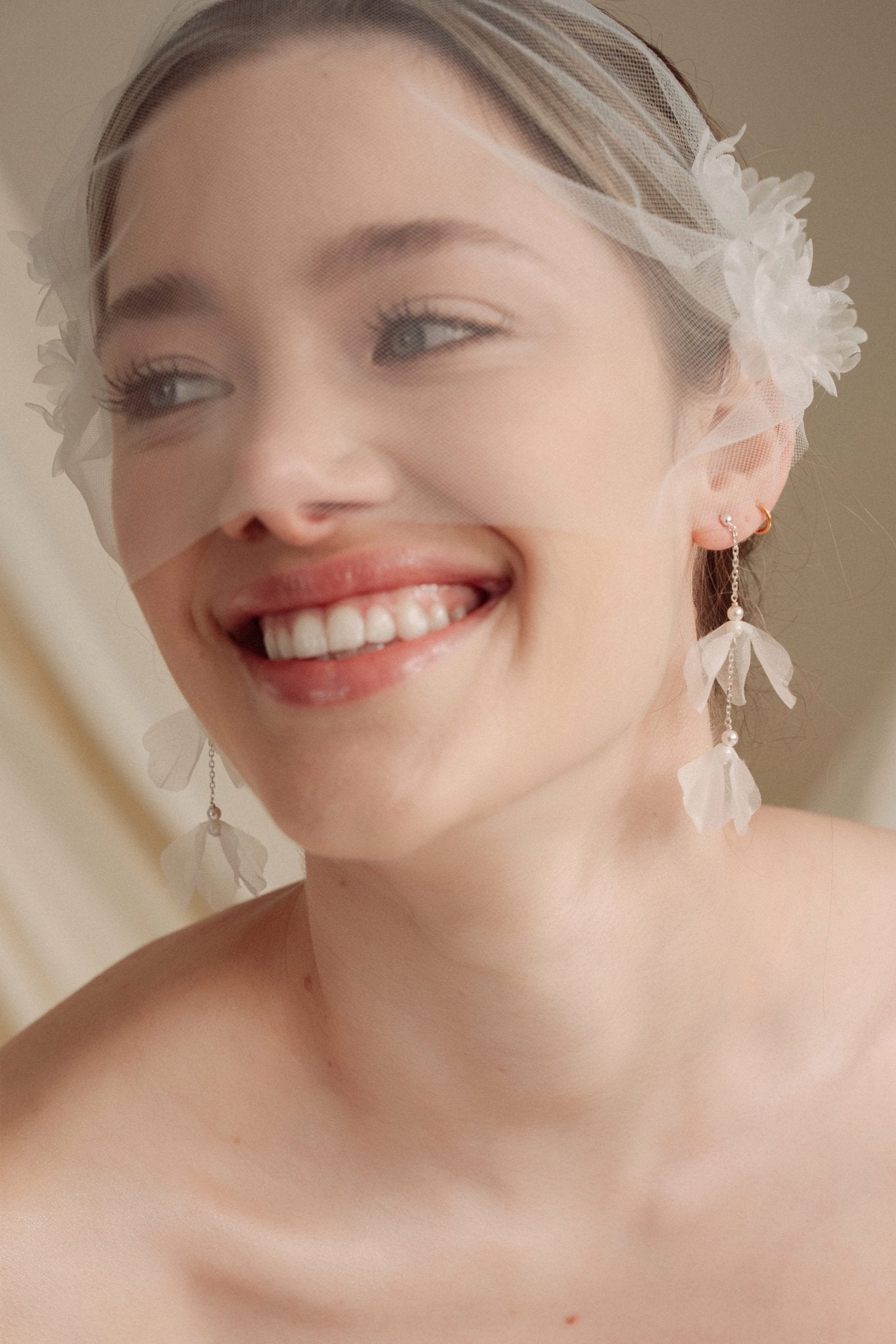 Bride wears an ivory tulle veil with face-framing silk flowers with coordinating silk flower and pearl long drop earrings