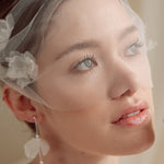 Bride wears an ivory tulle veil with face-framing silk flowers with coordinating silk flower and pearl long drop earrings