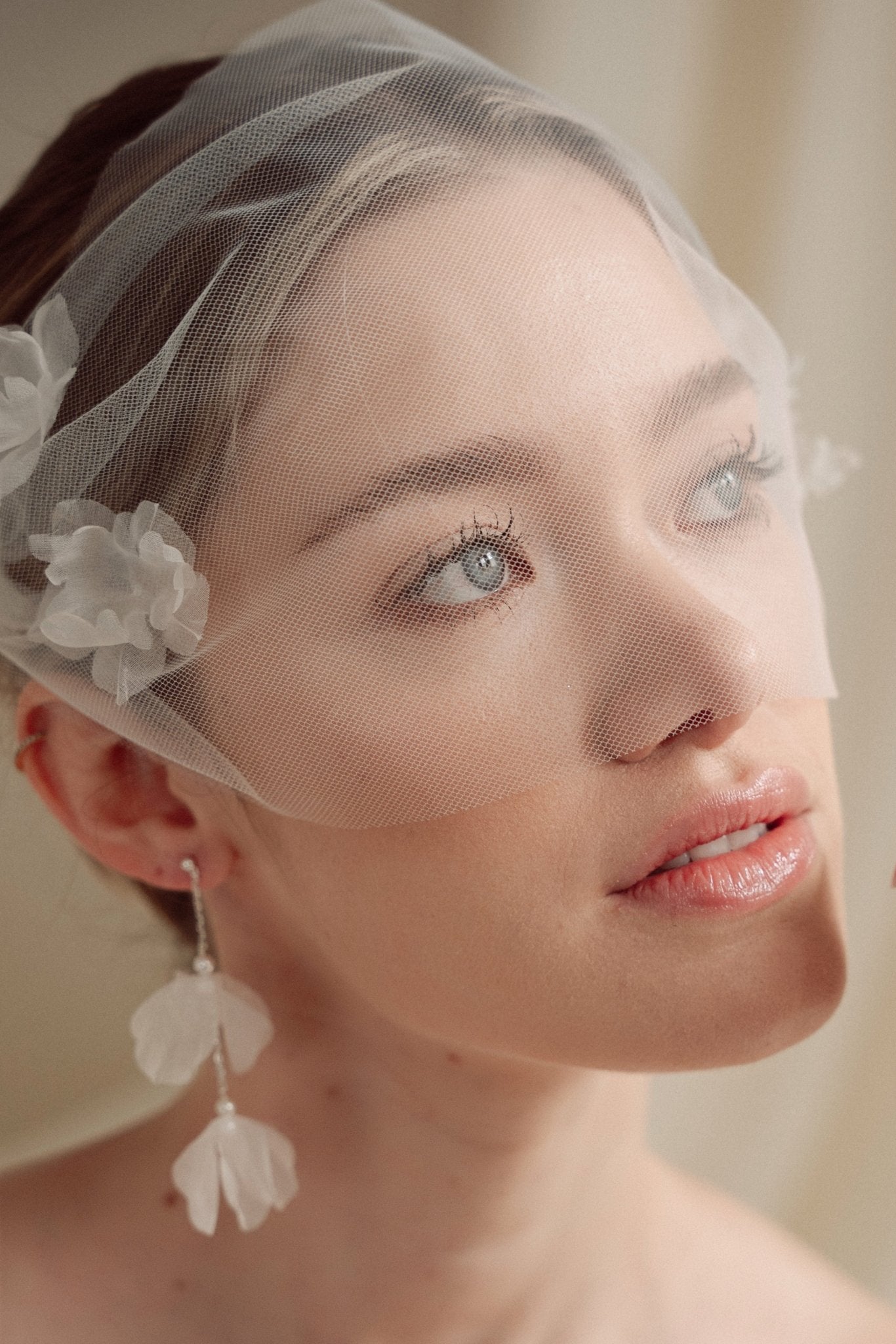 Bride wears an ivory tulle veil with face-framing silk flowers with coordinating silk flower and pearl long drop earrings
