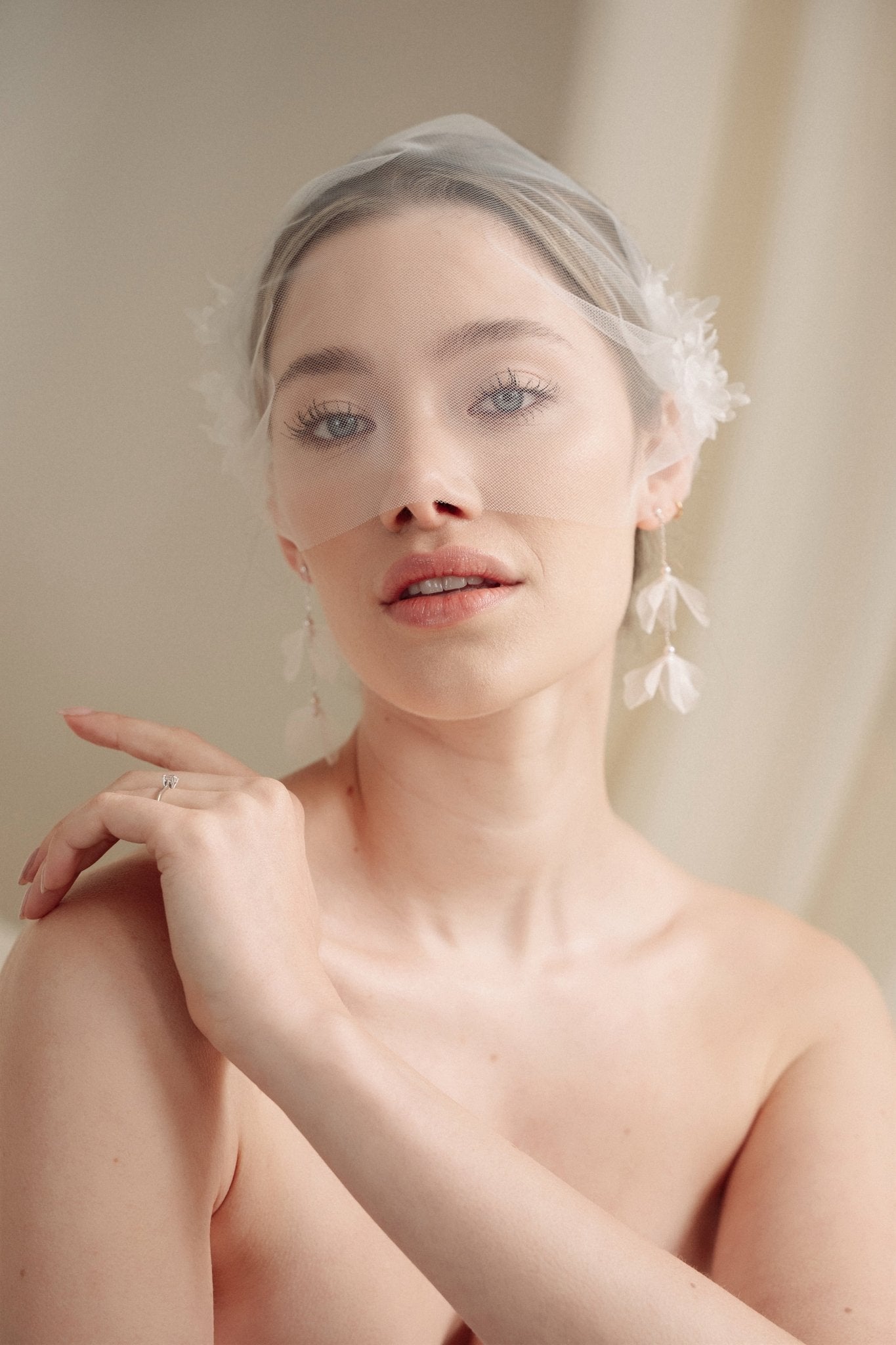 Bride wears an ivory tulle veil with face-framing silk flowers with coordinating silk flower and pearl long drop earrings