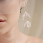 Bride wears an ivory tulle veil with face-framing silk flowers with coordinating silk flower and pearl long drop earrings